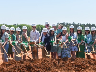 A group of people holding shovels. They are standing over dirt and smiling.