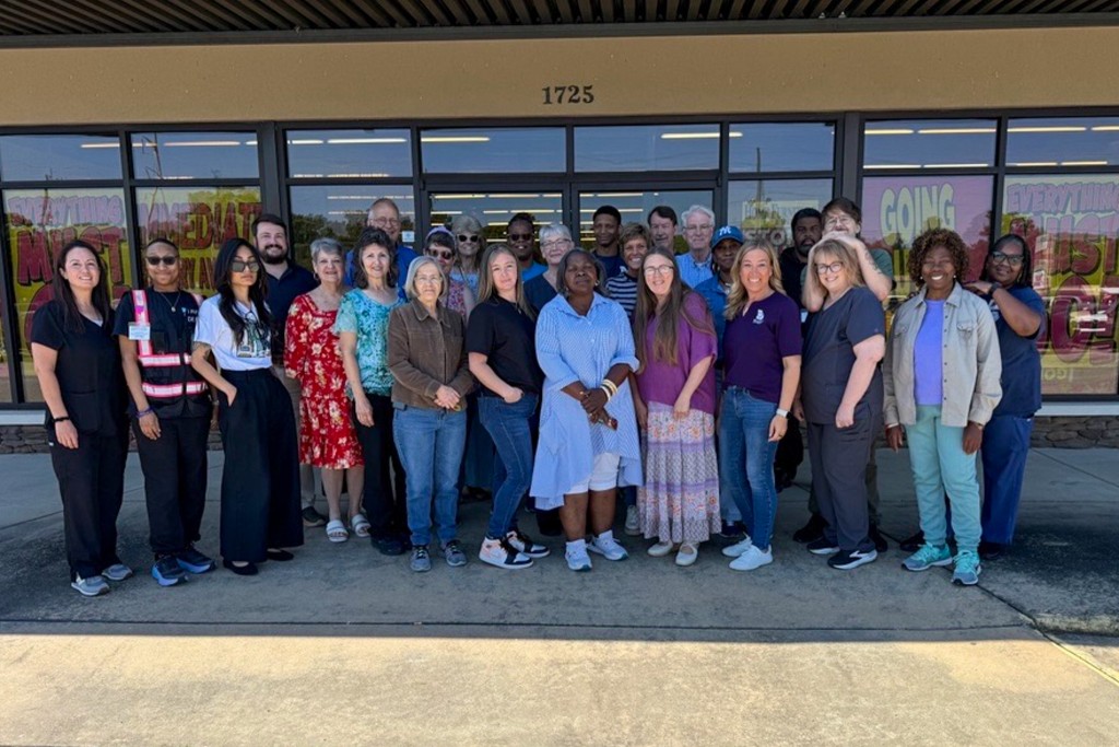 A group of people standing in front of a building. They are smiling.
