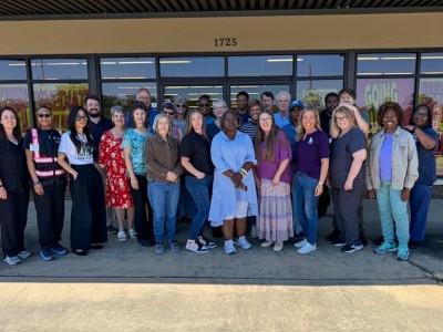 A group of people standing in front of a building. They are smiling.