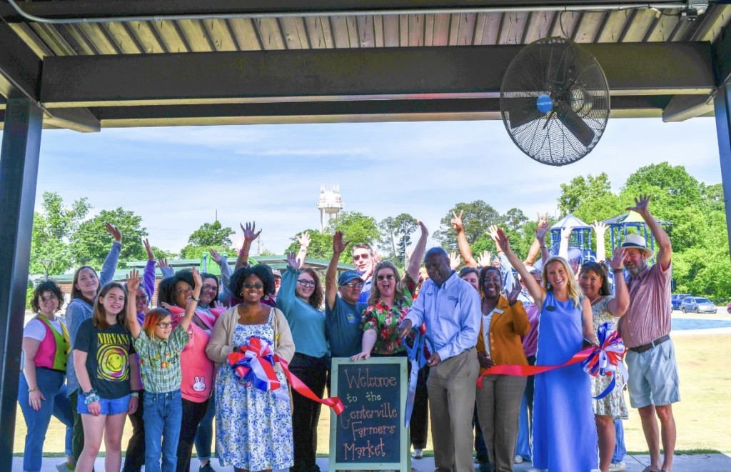 A group of people holding their hands up, smiling. There is a red ribbon in front of them. 