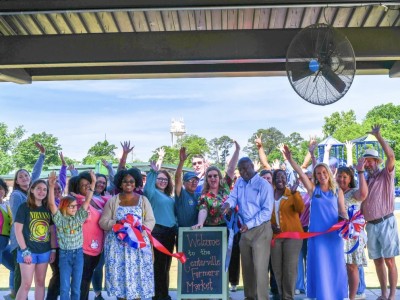 A group of people holding their hands up, smiling. There is a red ribbon in front of them.