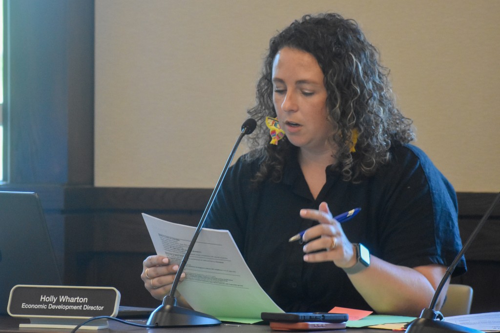 A woman in a black dress sitting behind a desk. She is reading something off a piece of paper. 
