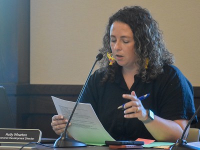 A woman in a black dress sitting behind a desk. She is reading something off a piece of paper.