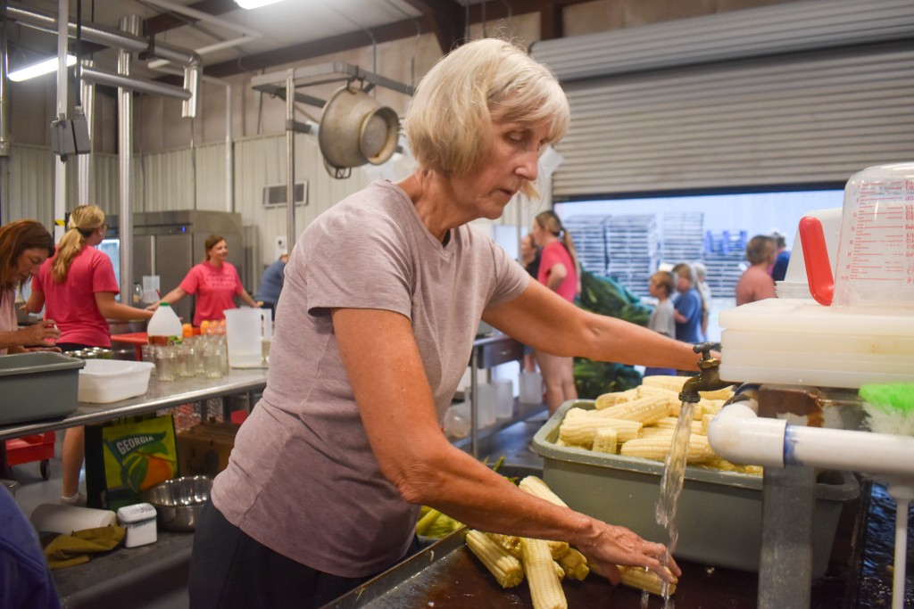 An older woman in a purple shirt washing her hands. 