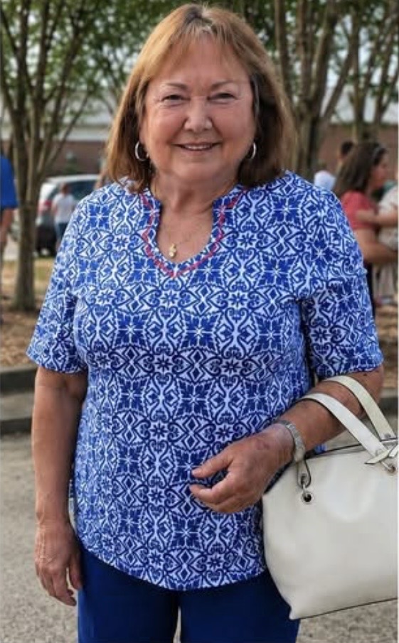 A white woman in a blue shirt. She has brown hair and is smiling.
