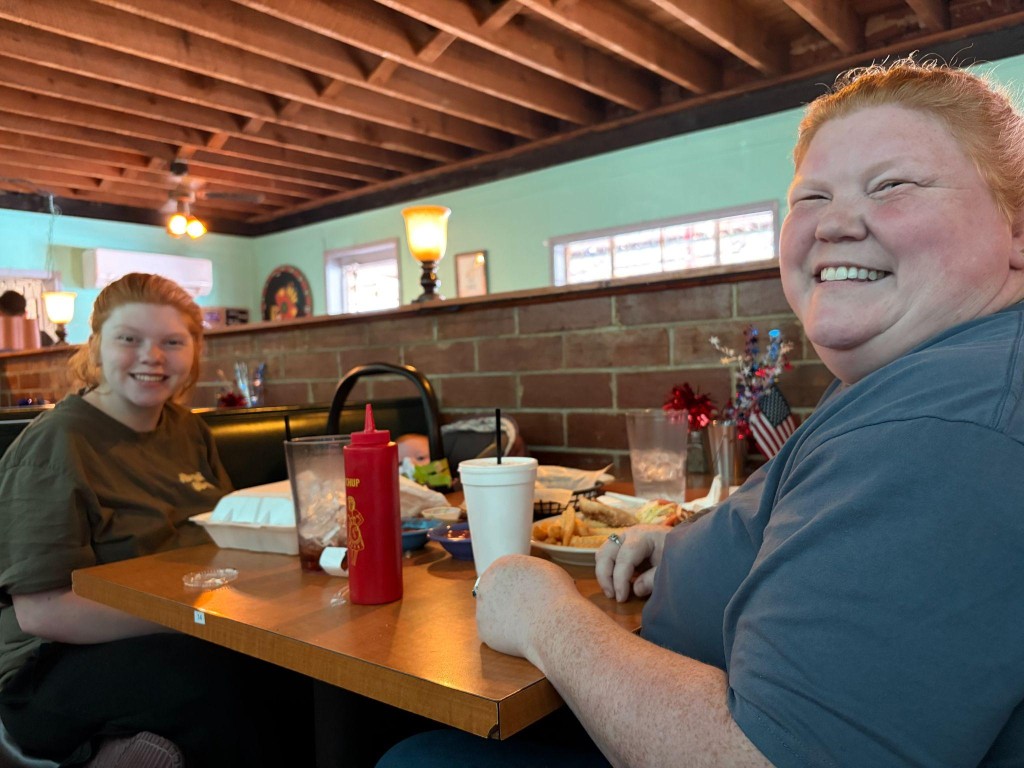 A longtime customer and her daughter sit in a restaurant booth, smiling as they enjoy their meal.