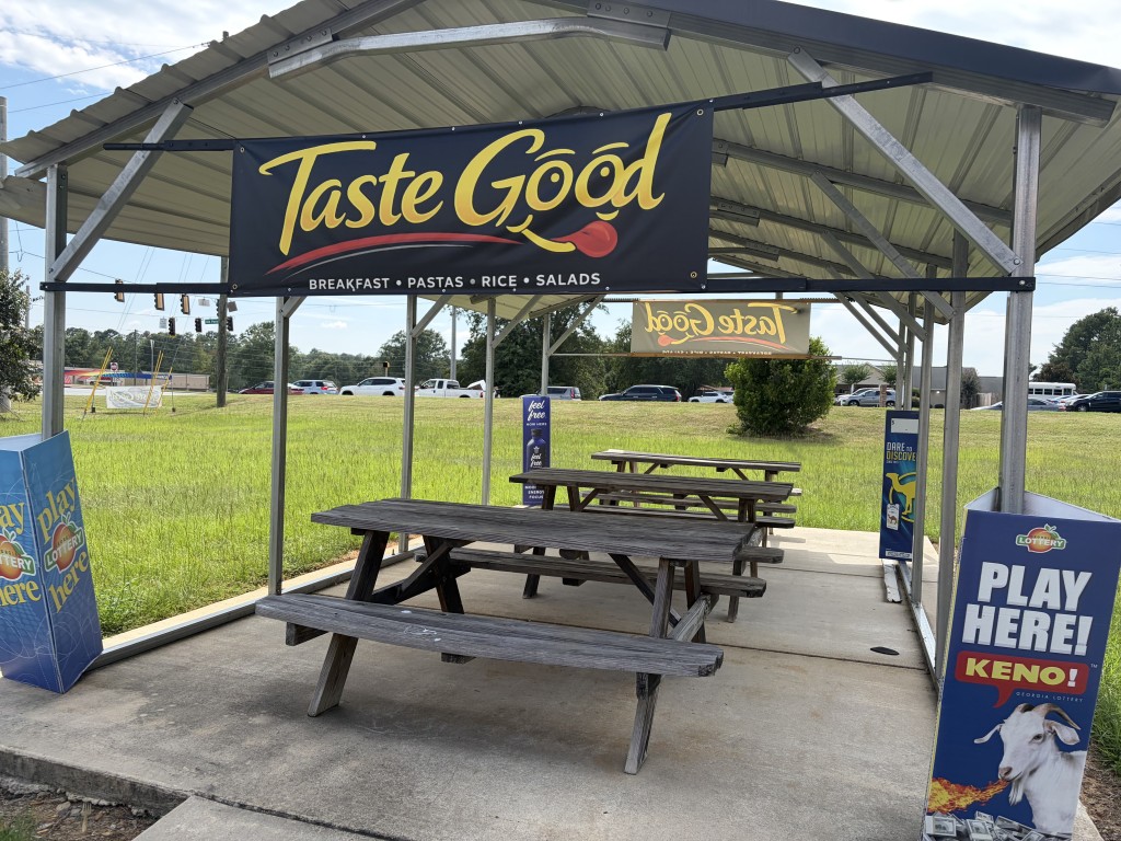 Panic pavilion with three picnic tables with the Taste Good Restaurant logo hanging across the top of the structure in the foreground.