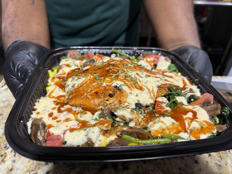 Photo shows arms and hands of restaurant owner holding up a salmon over rice dish.