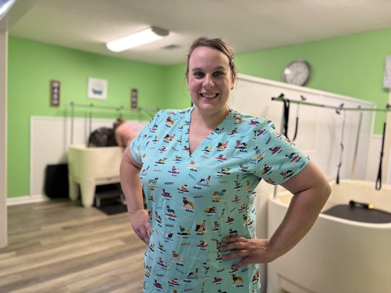 Owner of new DIY dog wash & grooming business poses for a photo with the dog washing and grooming area in the background.