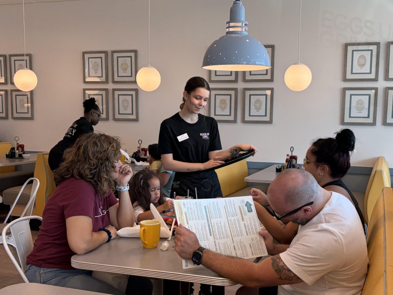 Server takes order from family seated in the restaurant with yellow booths, blue lights and white clear lamps hanging from the ceiling.