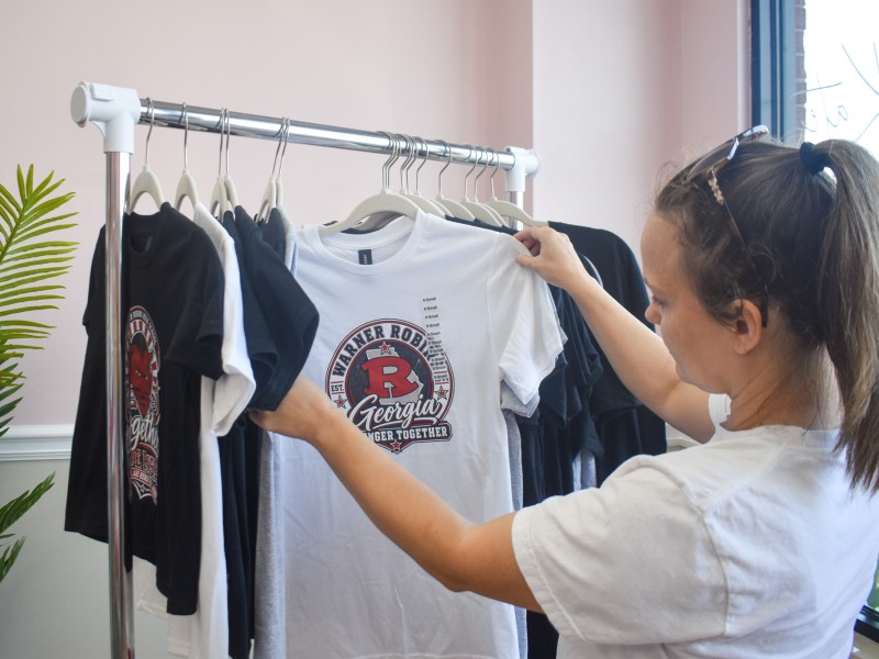 A women in a white shirt looking at a white shirt with a design on it.
