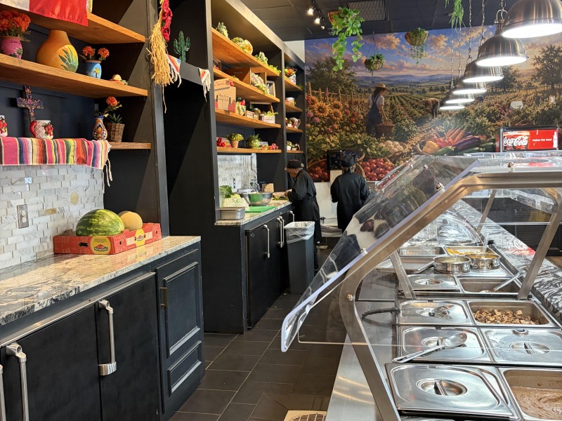 A long buffet with Mexican food with Mexican flags and memorabilia on the back wall of the restaurant.