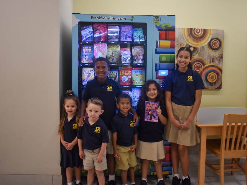 A group of students standing in front of the vending machine smiling.