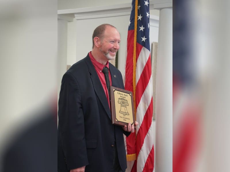 An older man in a suit holding a gold plaque.