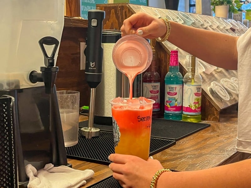 A pink and orange drink being poured into a cup