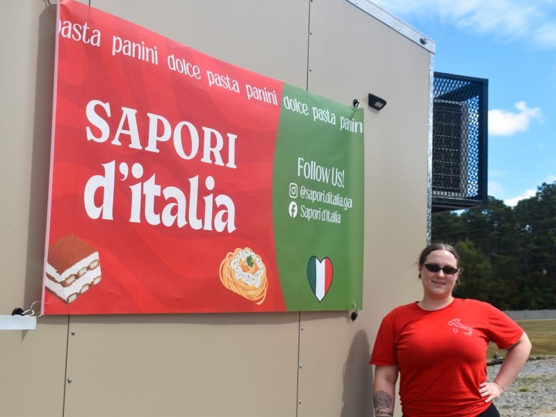 A women in a red shirt standing next to a red and green sign with white lettering.